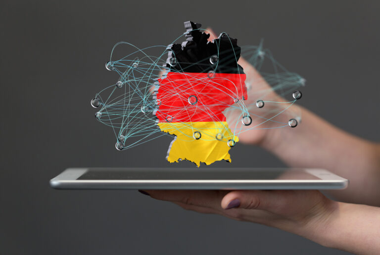 Composit: Hände halten ein Tablet, darüber schwebt ein 2D-Objekt mit den Umrissen und Farben von Deutschland, überlagert von einem gezeichneten Netzwerk.