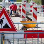 Straßenbaustelle mit Absperrbaken und einem Verkehrsschild, das Bauarbeiten signalisiert.