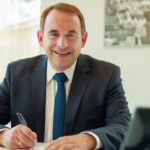 Porträt von Hessens Finanzminister Professor Dr. R. Alexander Lorz, anscheinend in seinem Büro etwas mit der Hand schreibend.