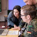 Personen in Bundeswehruniformen sitzen in einem Büro vor einem Computermonitor.