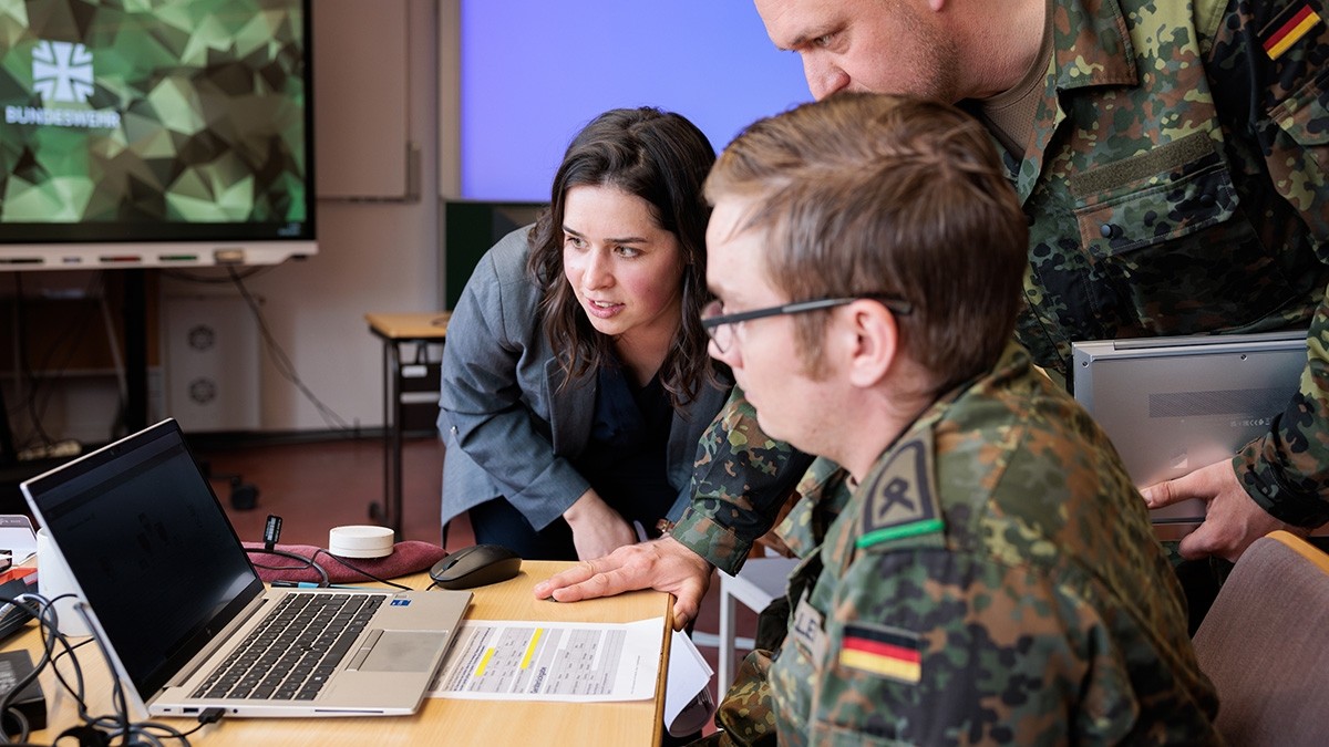 Personen in Bundeswehruniformen sitzen in einem Büro vor einem Computermonitor.