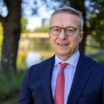 Bundesdigitalminister Karsten Wildberger, im Schatten unter Bäumen, im Hintergrund ein Kanal.