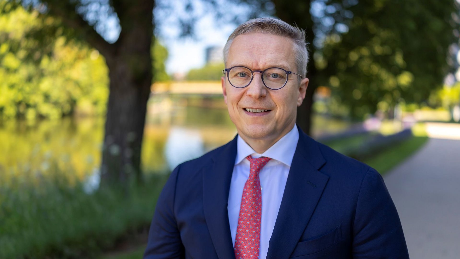 Bundesdigitalminister Karsten Wildberger, im Schatten unter Bäumen, im Hintergrund ein Kanal.