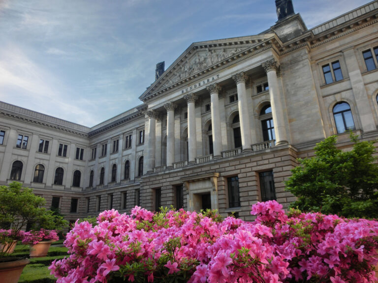 Außenansicht des klassizistischen Bundesratsgebäudes, im Vordergrund blühender Rhododendron.