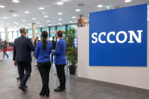 Blick in den Eingangsbereich: Man sieht mehrere Aufsteller mit der Aufschrift "SCCON" sowie drei Personen, die mit dem Rücken zur Kamera stehen.