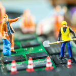 Miniaturfiguren von Bauarbeitern stehen auf einem Motherboard und "arbeiten".