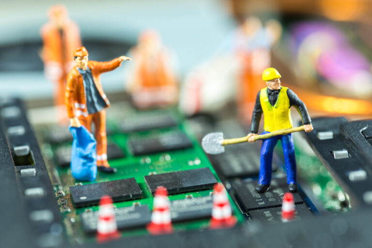 Miniaturfiguren von Bauarbeitern stehen auf einem Motherboard und "arbeiten".