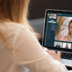 Blick über die Schulter einer jungen Frau, auf deren Laptop eine Videokonferenz läuft.