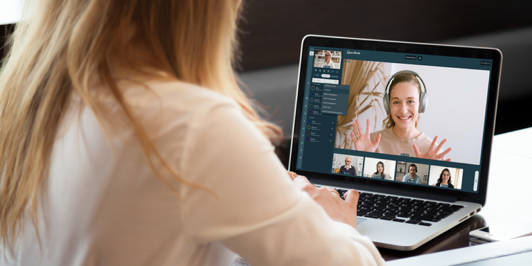 Blick über die Schulter einer jungen Frau, auf deren Laptop eine Videokonferenz läuft.