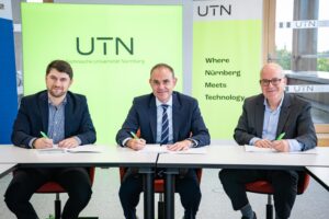 Drei Männer in Anzügen und Stiften in den Händen sitzen an einem Tisch, vor sich Papiere.