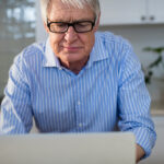 Älterer Mann in häuslicher Umgebung mit Laptop