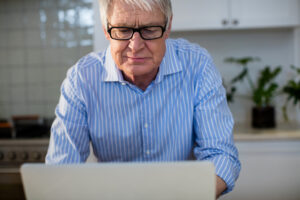 Älterer Mann in häuslicher Umgebung mit Laptop