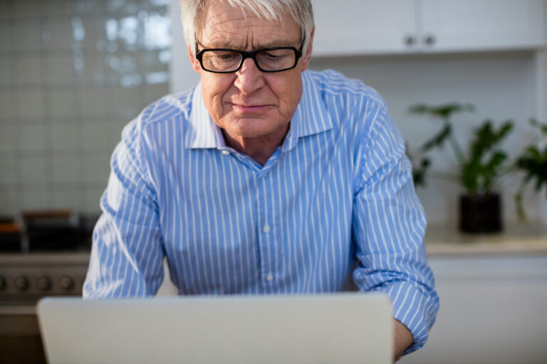 Älterer Mann in häuslicher Umgebung mit Laptop