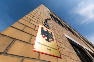 Hauptsitz des ITZBund in Bonn – Blick aus der starken Froschperspektive auf die ockerfarbene Klinkerfassade und Messingschild mit Bundesadler.