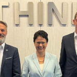 Zwei Männer und eine Frau in formaler Kleidung stehen lächelnd aufgereiht vor einer Wand mit dem Wort "Think".
