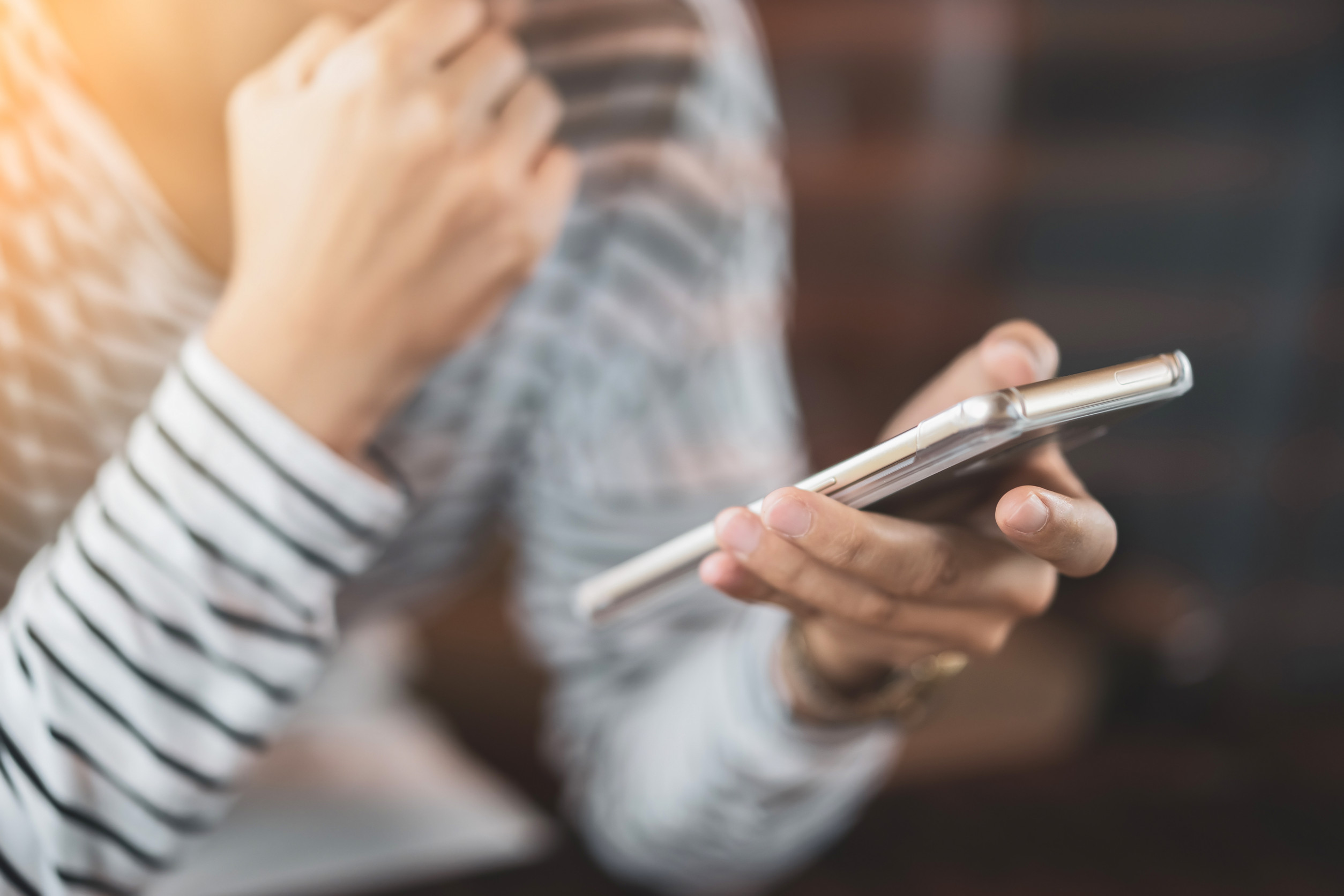 Hände und Torso einer mutmaßlich weiblichen Person, die mit nachdenklicher Pose ein Smartphone hält.