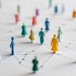 Eine Gruppe von Papierfiguren in verschiedenen Farben, dazwischen Linien, die soziale Verbindungen und Interaktion darstellen.