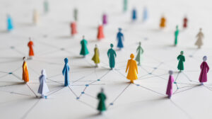 Eine Gruppe von Papierfiguren in verschiedenen Farben, dazwischen Linien, die soziale Verbindungen und Interaktion darstellen.