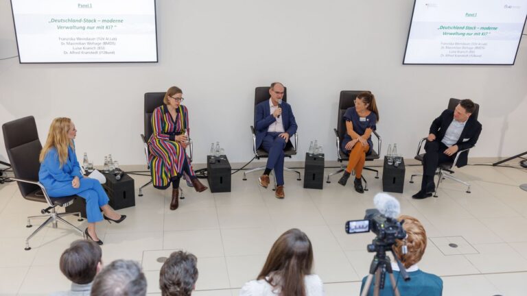 Aufsicht auf eine Personengruppe, die in einem hellen, nüchternen Raum in einem Stuhlkreis sitzt.