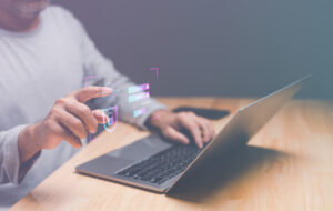 Laptop mit Schreibtischplatte, Händen und Oberkörper einer person. Overlay mit "Security"-Icons.