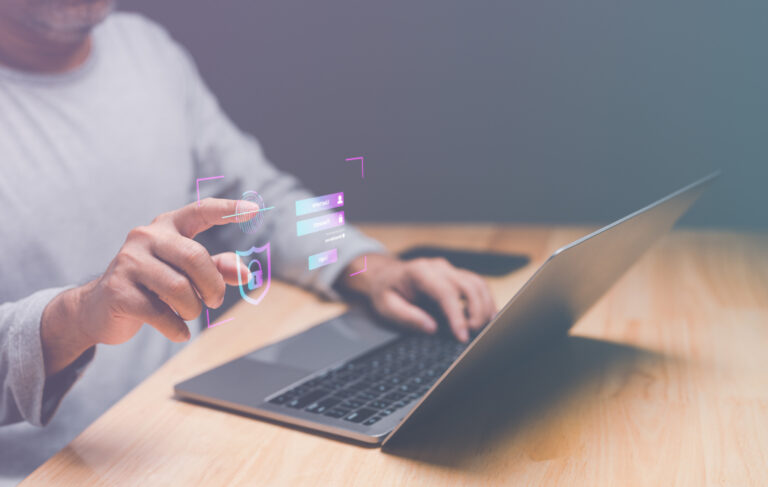 Laptop mit Schreibtischplatte, Händen und Oberkörper einer person. Overlay mit "Security"-Icons.