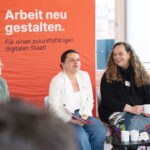 Drei Frauen sitzen vor einem Plakat mit der Aufschrift "Arbeit neu gestalten"