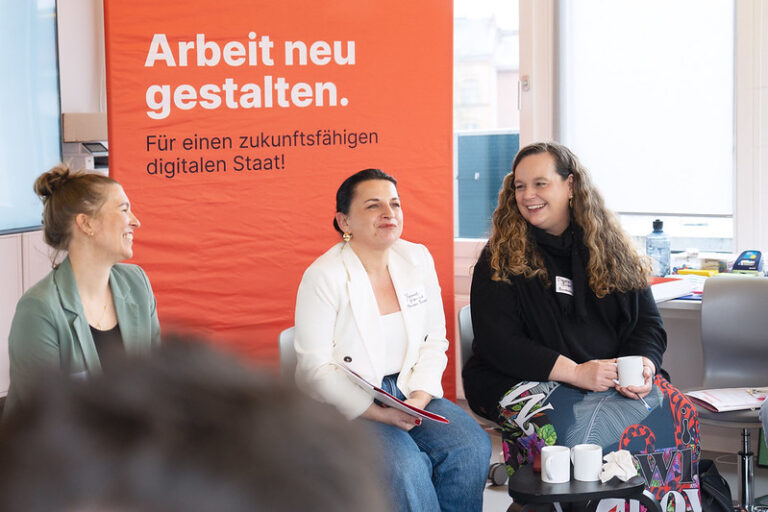 Drei Frauen sitzen vor einem Plakat mit der Aufschrift "Arbeit neu gestalten"