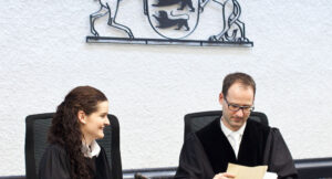 Richterin und Richter im Hintergrund das Landeswappen BW