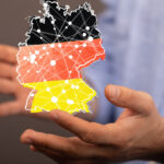 Person mit hellem Hemd hält virtuelle Deutschlandkarte in schwarz-rot-gold in den Händen.