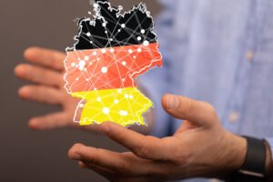 Person mit hellem Hemd hält virtuelle Deutschlandkarte in schwarz-rot-gold in den Händen.