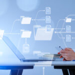 Composite in Blautönen: Geschäftsfrau tippt auf Smartphone, Laptop und Notebook auf einem Tisch. Overlay mit Ordnern mit Dokumentensymbolen.