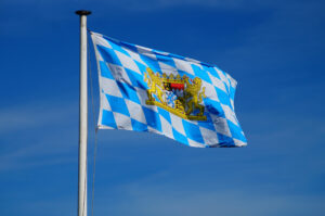 Bayernflagge (Rauten mit Wappen) vor blauem Himmel.