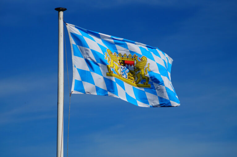 Bayernflagge (Rauten mit Wappen) vor blauem Himmel.
