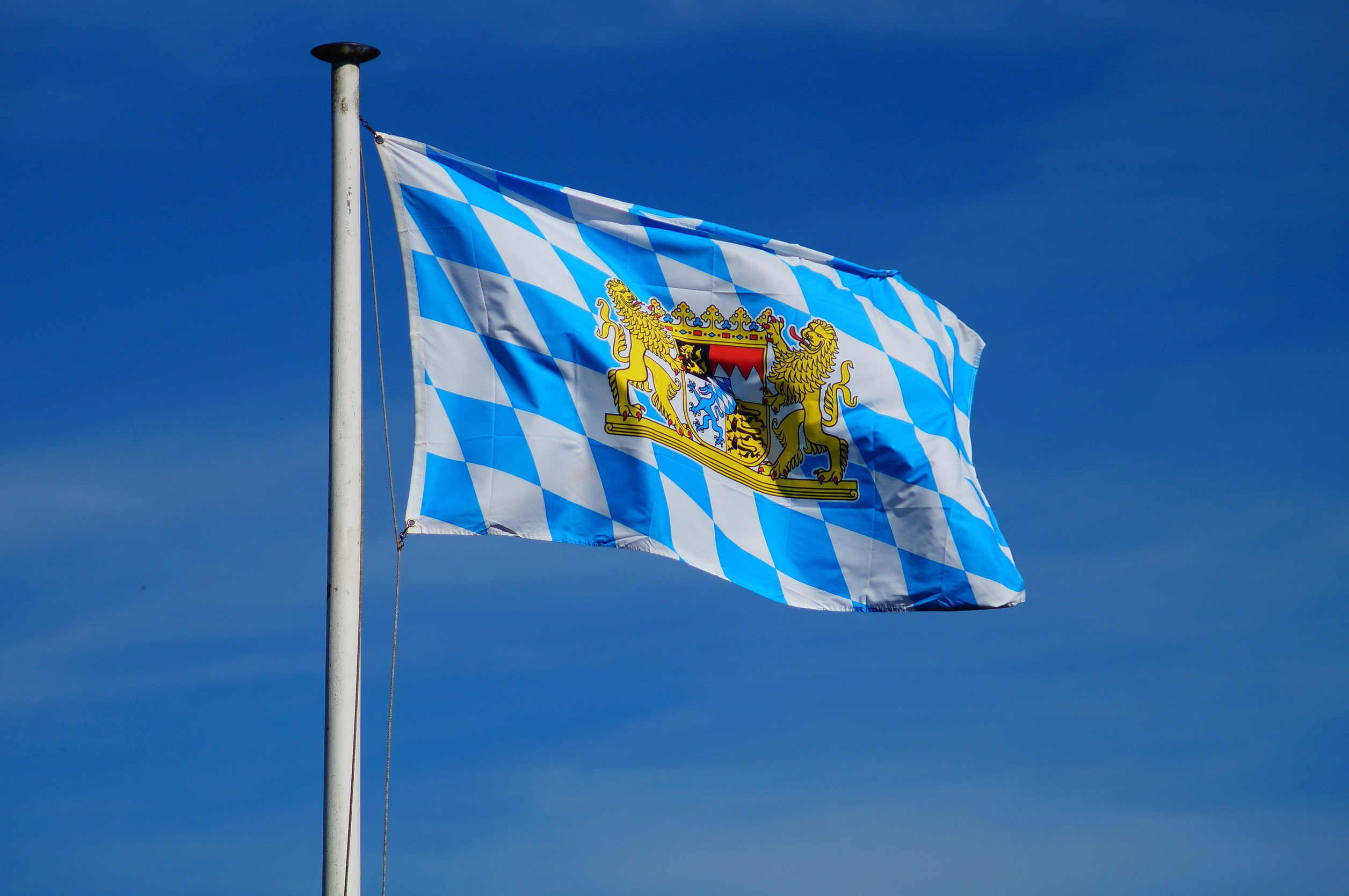 Bayernflagge (Rauten mit Wappen) vor blauem Himmel.