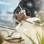 Montage: Schreibtisch, Laptops, Hände von Jacketttragenden Männern, Überlagerung mit diversen IT-Icons