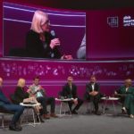 Purpurfarben ausgeleuchtetes Podium mit Diskususionsteilnehmenden auf Sesseln