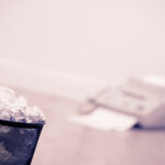 Papierkorb mit zusammengeknülten Papieren, im Hintergrund unscharf ein Fax-Gerät