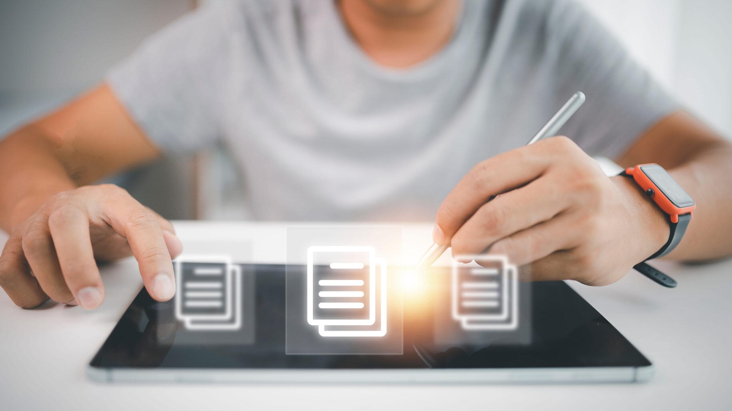 Eine jüngere Person sitzt über einem Tablet, über dem Dokumentensymbole schweben.