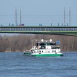  Binnenschiff fährt unter einer Brücke mit Solarpanelen hindurch.
