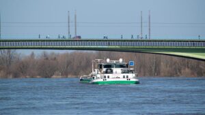  Binnenschiff fährt unter einer Brücke mit Solarpanelen hindurch.