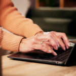 Laptop auf einem niedrigen Tisch in warmen Licht, Händet tippen darauf.