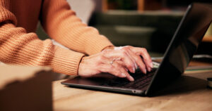 Laptop auf einem niedrigen Tisch in warmen Licht, Händet tippen darauf.