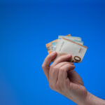 Hand mit Euronoten vor blauem Hintergrund