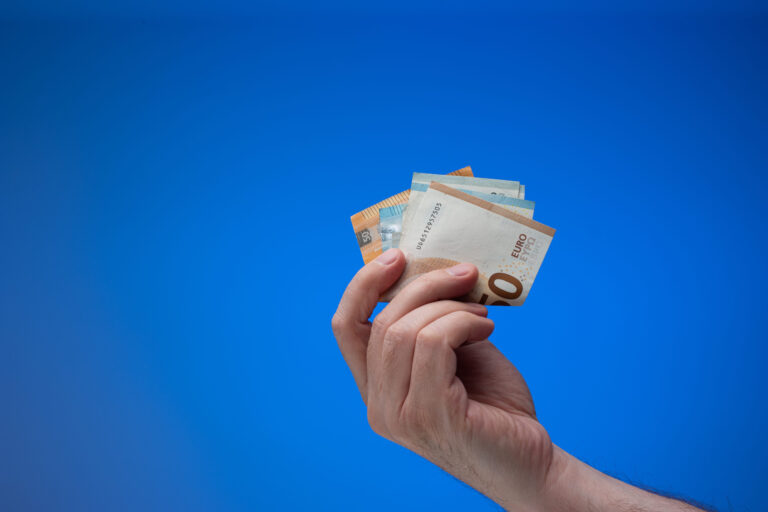 Hand mit Euronoten vor blauem Hintergrund