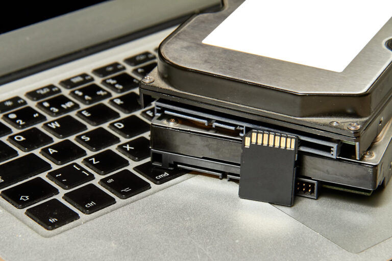 Stapel von verschiedenen IT-Speichermedien und ein aufgeklappter Laptop.