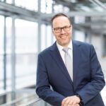 Sachsens Wirtschaftsminister Dirk Panter lächelnd auf ein Geländer eines modernen Stahl-Glas-Baues gelehnt