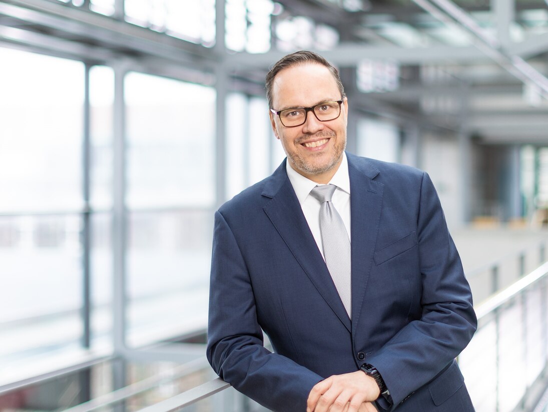 Sachsens Wirtschaftsminister Dirk Panter lächelnd auf ein Geländer eines modernen Stahl-Glas-Baues gelehnt