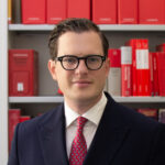 Der designierte BfDI Moritz Hennemann im Porträt vor Bücherregal mit Gesetzestexten.