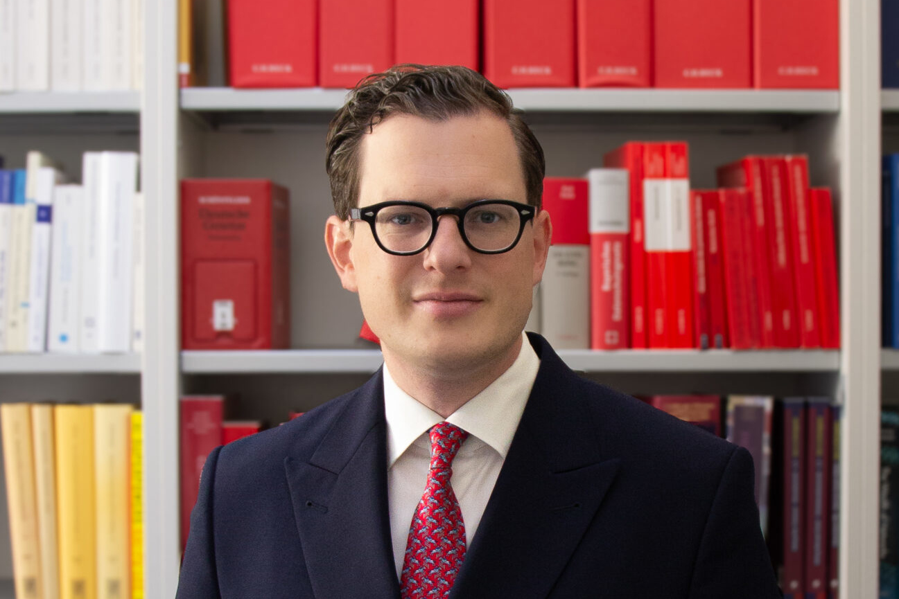Der designierte BfDI Moritz Hennemann im Porträt vor Bücherregal mit Gesetzestexten.