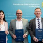 Drei steif lächelnde Menschen stehen nebeneinander vor einer blauen Wand und halten Doklumentenmappen in ihren Händen.